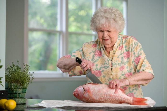 Starsza pani kroi rybę dużym kuchennym nożem