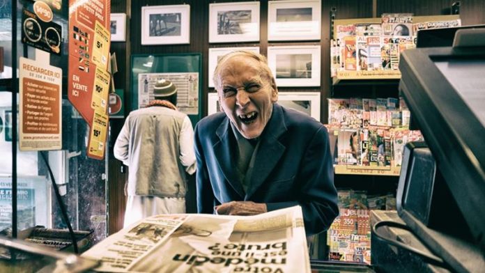 Uśmiechnięty starszy pan w garniturze wybiera gazetę w saloniku prasowym